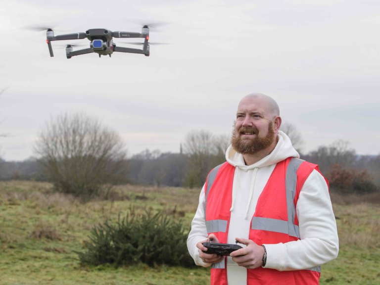A profile picture of Chris Vaughan, owner of Chris Vaughan Photography, flying a drone. Chris is wearing a white hoodie and a high-vis jacket that has drone pilot written on the back.
