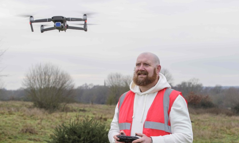 A profile picture of Chris Vaughan, owner of Chris Vaughan Photography, flying a drone. Chris is wearing a white hoodie and a high-vis jacket that has drone pilot written on the back.