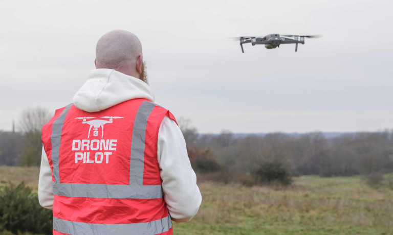 A profile picture of Chris Vaughan, owner of Chris Vaughan Photography, flying a drone. Chris is wearing a white hoodie and a high-vis jacket that has drone pilot written on the back.