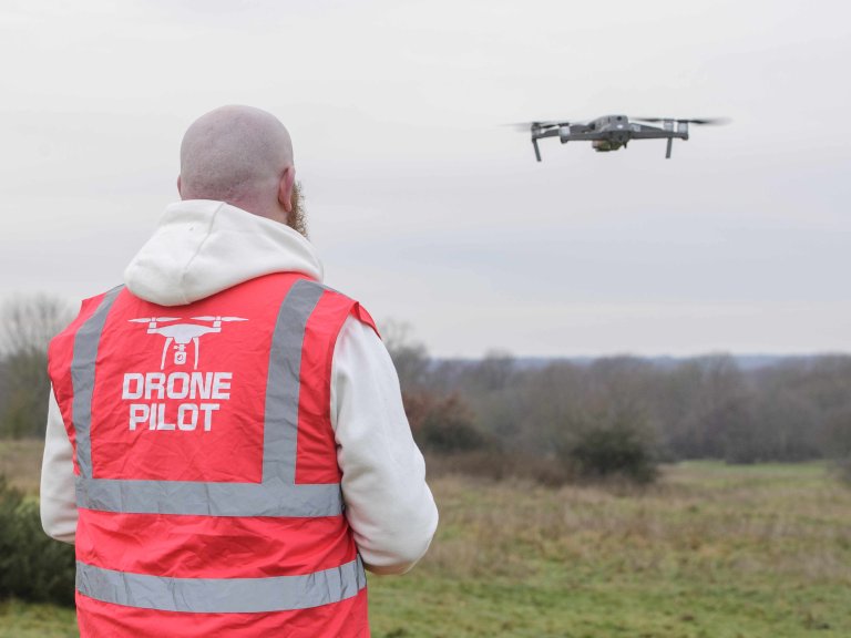 A profile picture of Chris Vaughan, owner of Chris Vaughan Photography, flying a drone. Chris is wearing a white hoodie and a high-vis jacket that has drone pilot written on the back.