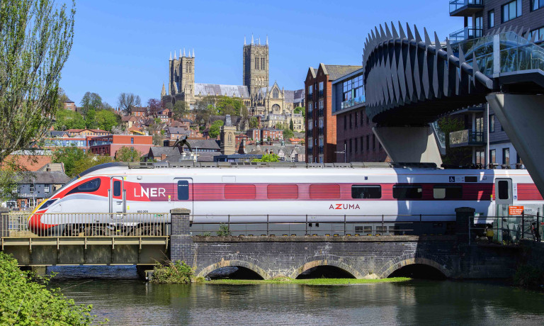 An LNER Azuma train arriving at Lincoln Central train station with Lincoln Cathedral in the background.