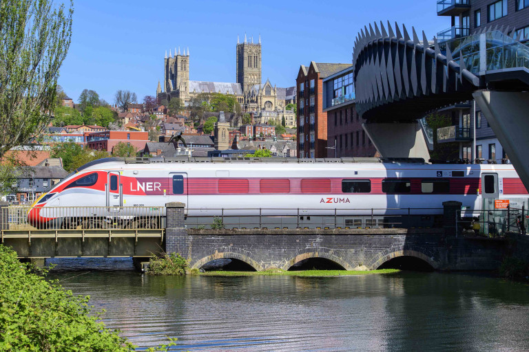 An LNER Azuma train arriving at Lincoln Central train station with Lincoln Cathedral in the background.